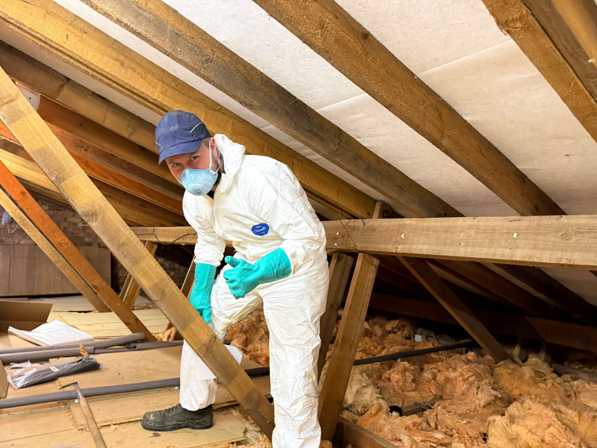 Pest control technician in protective PPE working in loft during rat infestation clean-up and insulation removal