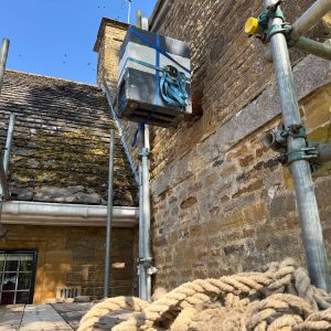 How Much Do Live Honeybee Removals From Buildings Cost? this image shows a live honeybee removal from a home. There is a scafffolding erected to the outside of the building with a nuc in place to house the bees